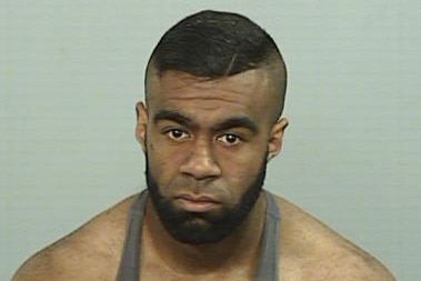A mugshot of a man wearing a singlet and looking glum