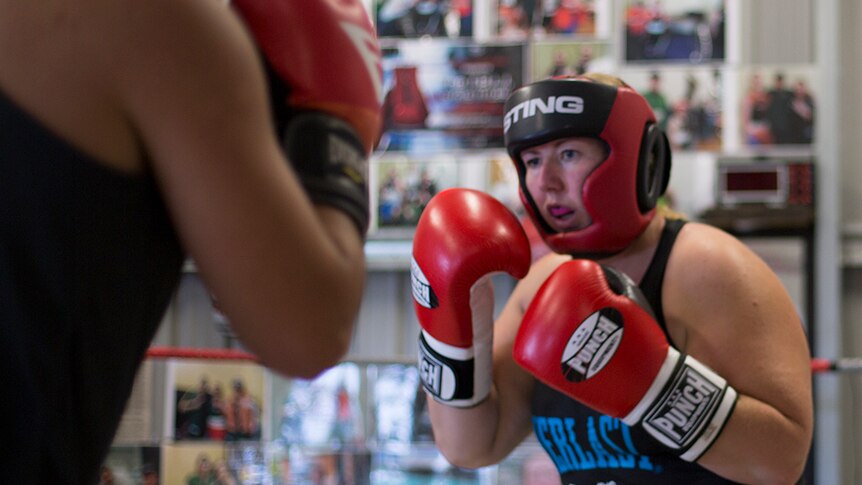 A female boxer spars with a partner in the boxing gym.