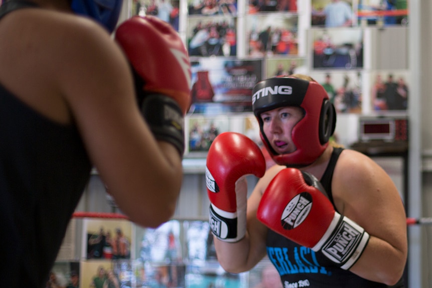 A female boxer spars with a partner in the boxing gym.