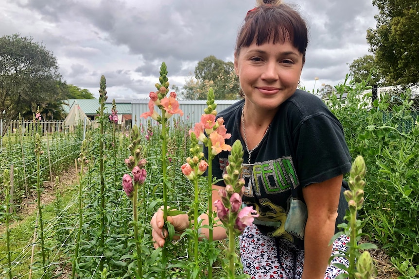 A young woman crouches near a row of colourful snapdragons.