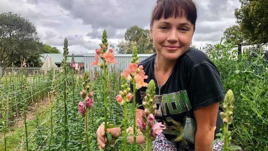 A young woman crouches near a row of colourful snapdragons.