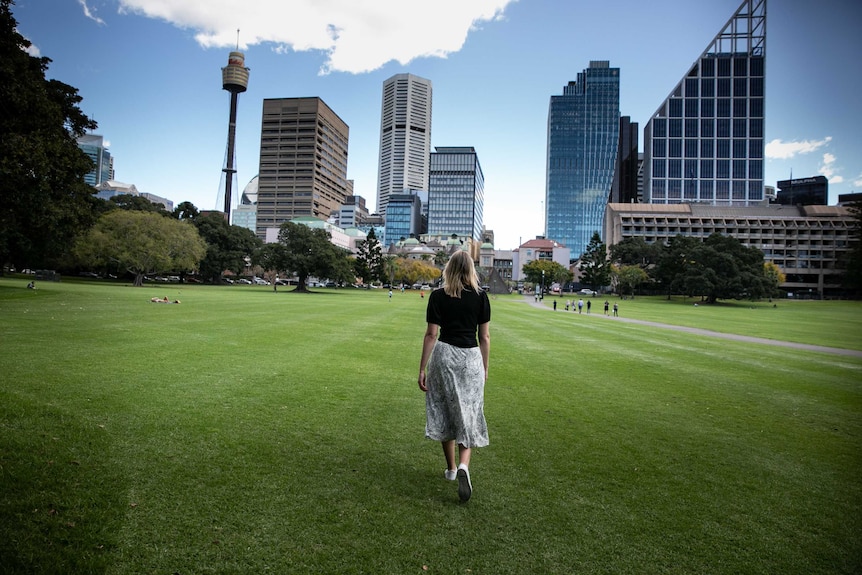 A woman with her back to the camera, walking on grass