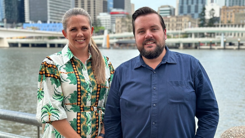 A woman wearing a dress and a man wearing a blue shirt standing in front of the Brisbane River.