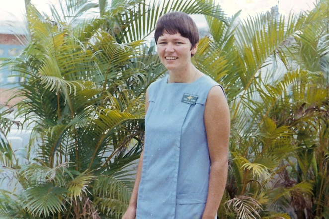 A woman in blue nurse uniform in front of palm trees