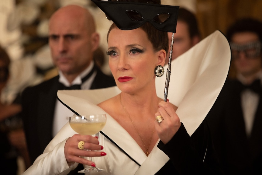 Film still of Emma Thompson as The Baroness in a structured dress with a martini glass and an eye mask in Cruella