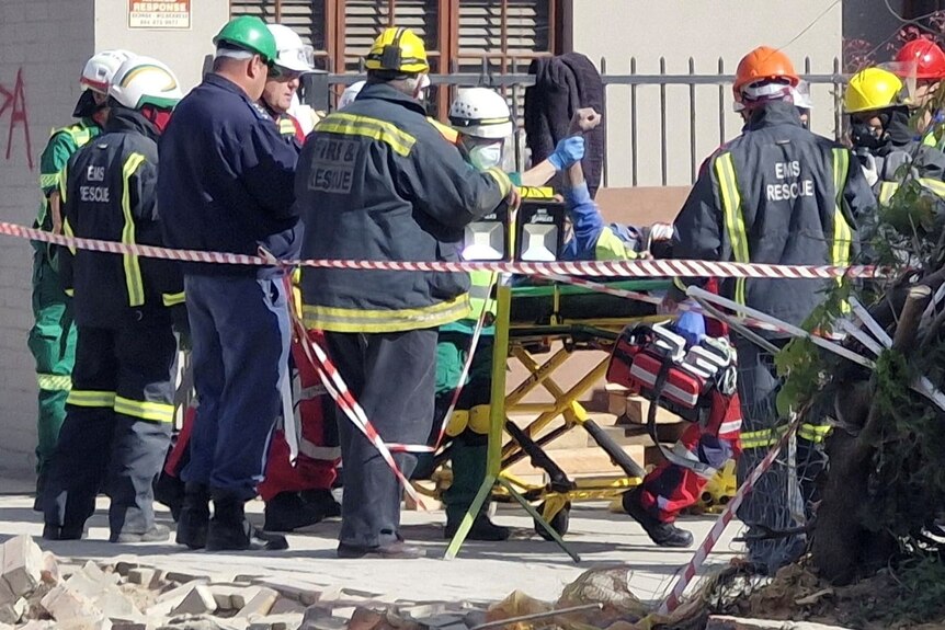 A man on a stretcher surrounded by emergency workers. One worker is holding the man's arm in the air.