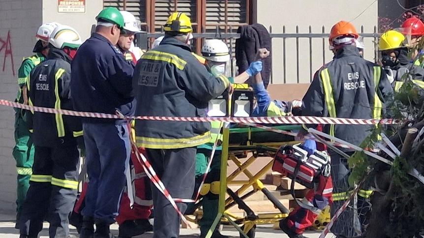 A man on a stretcher surrounded by emergency workers. One worker is holding the man's arm in the air.
