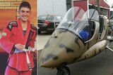 A young man in a martial arts outfit next to a photo of a gyrocopter painted in camouflage design.