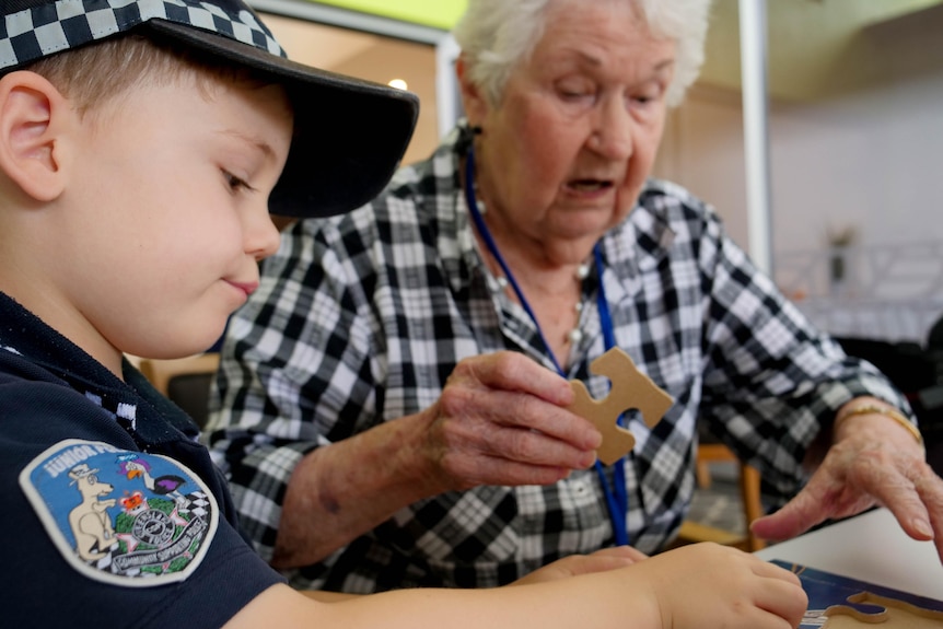 An older woman in a checked shirt doing a puzzle with a young boy wearing a police uniform.