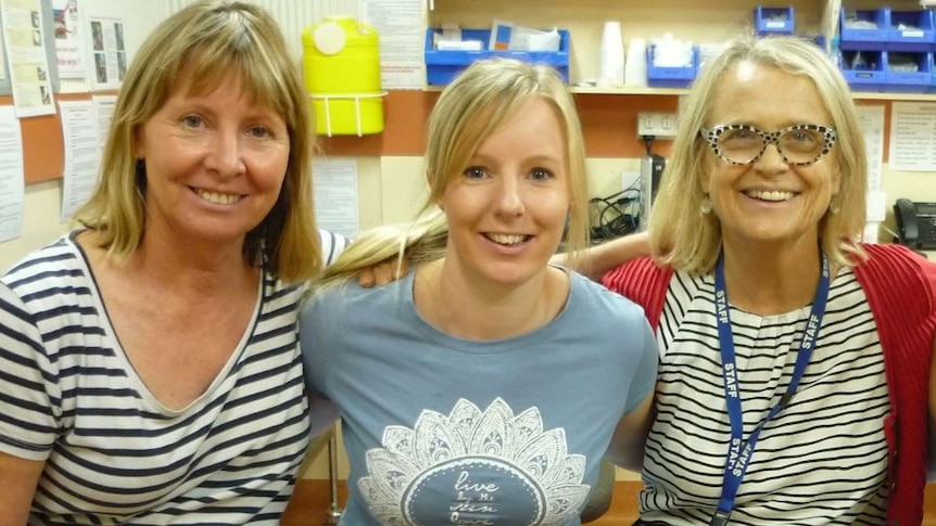 Three women stand alongside each other, smiling