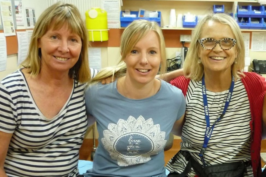 Three women stand alongside each other, smiling