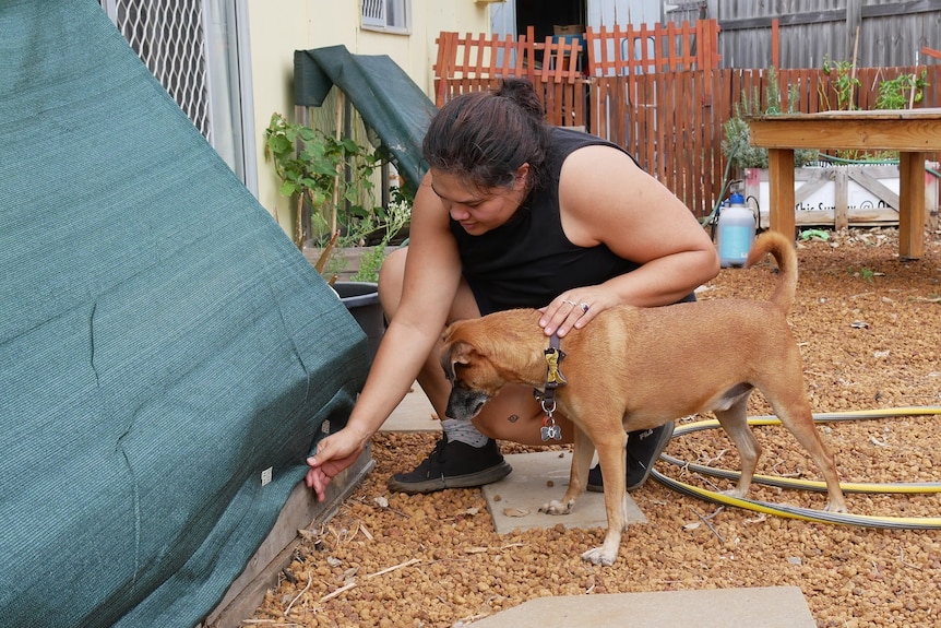 Dark-haired woman kneels near home while patting dog