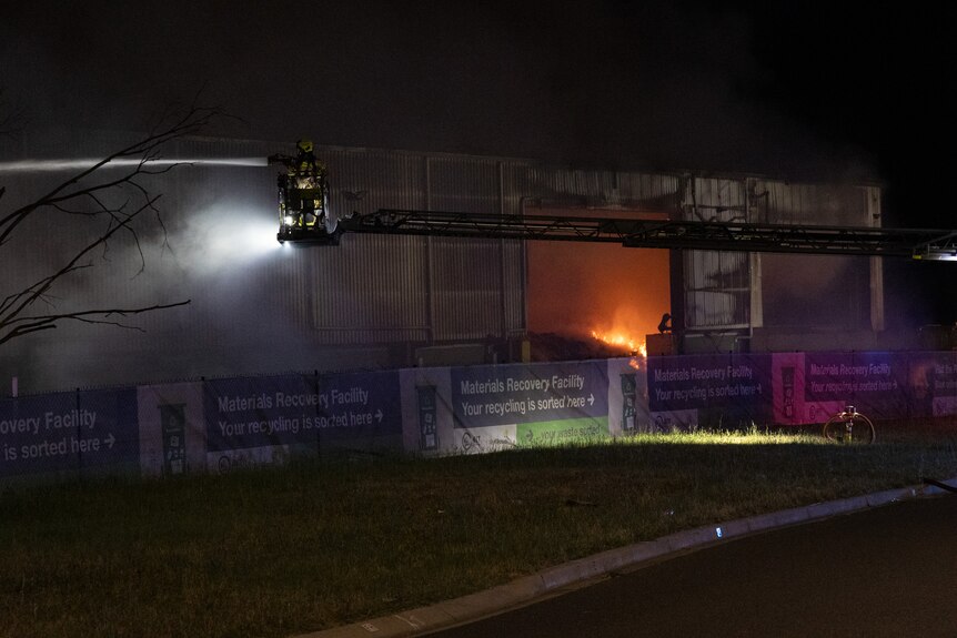 A fire burns in a large warehouse at nighttime.