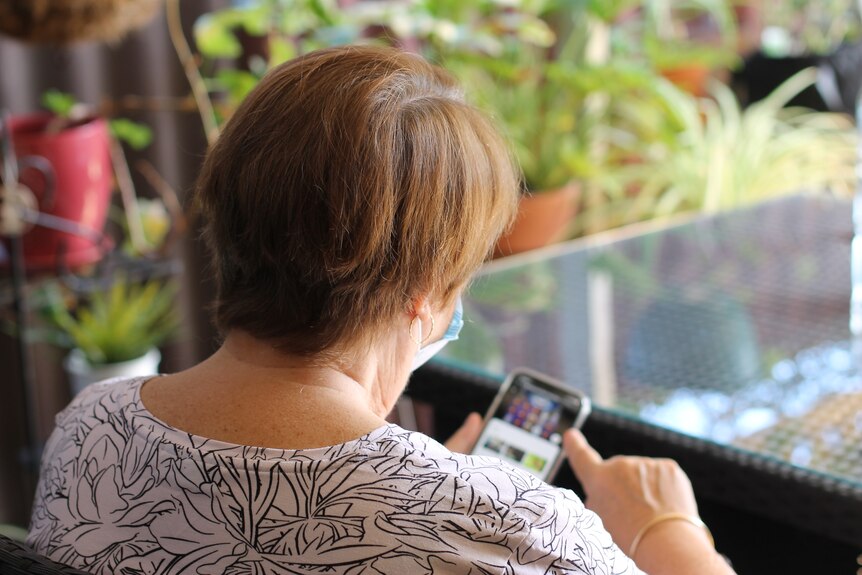 Back of woman's head, looking at screen of i phone in her hand.