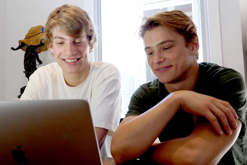 Two young men looking at a laptop computer in front of them.