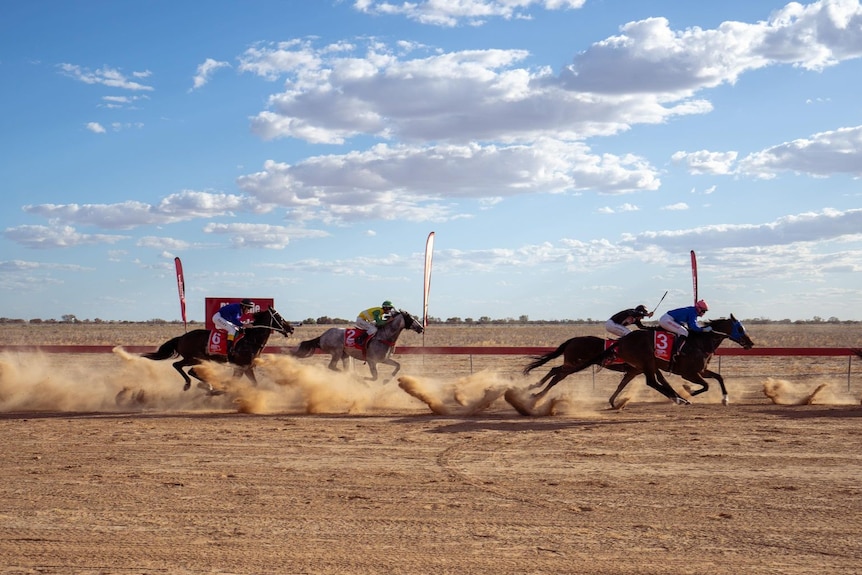 Jockeys on horses crossing the finish line on dirt race track