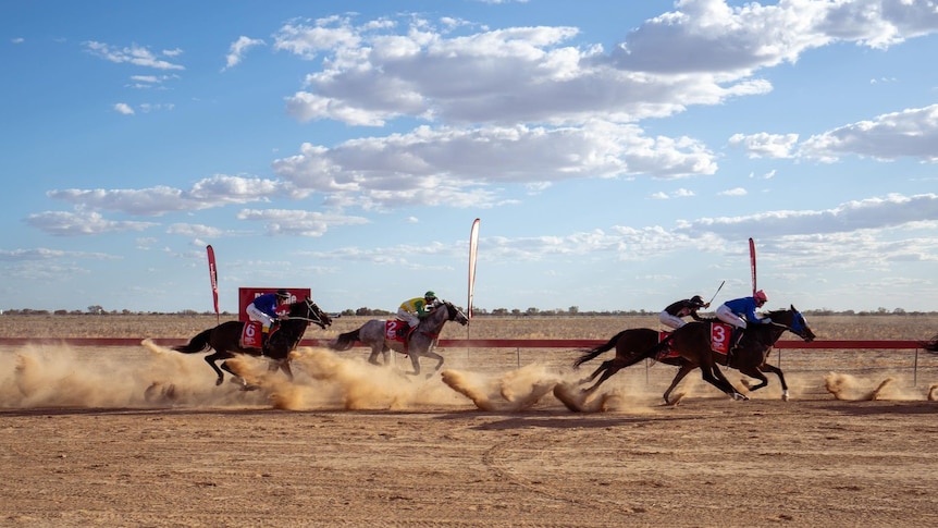 Jockeys on horses crossing the finish line on dirt race track