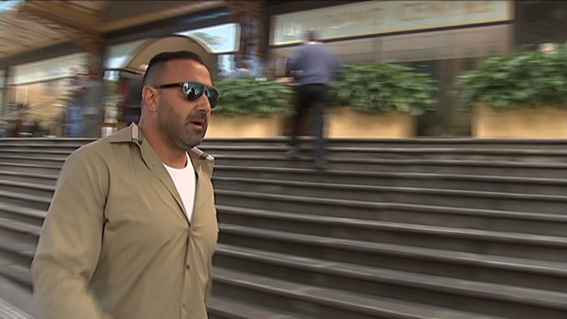 Man in sunglasses and khaki shirt with stairs in the background