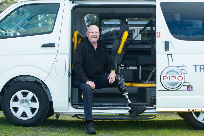 A man with a prosthetic leg relaxes inside the open side door of a commercial van