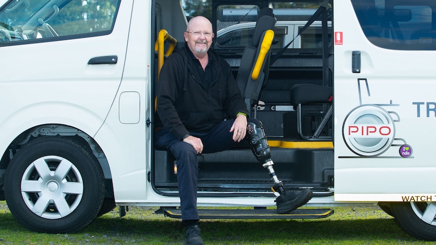 A man with a prosthetic leg relaxes inside the open side door of a commercial van