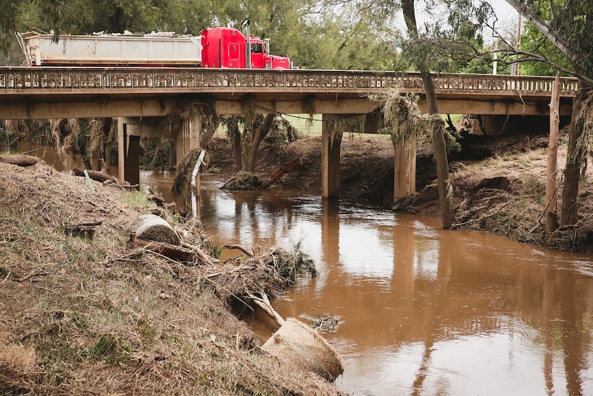 A bridge with a creek running under it and a truck driving over.