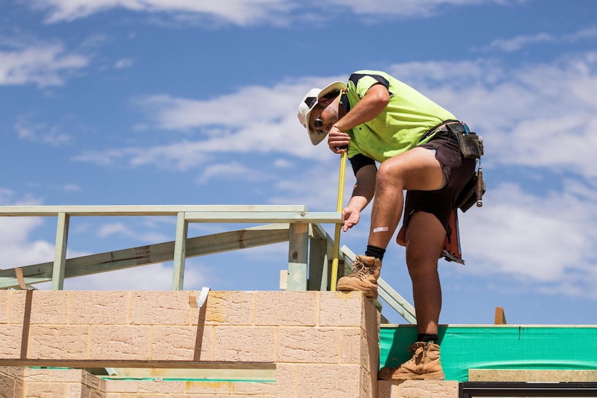 A carpenter with a tape measure works on a roof.  