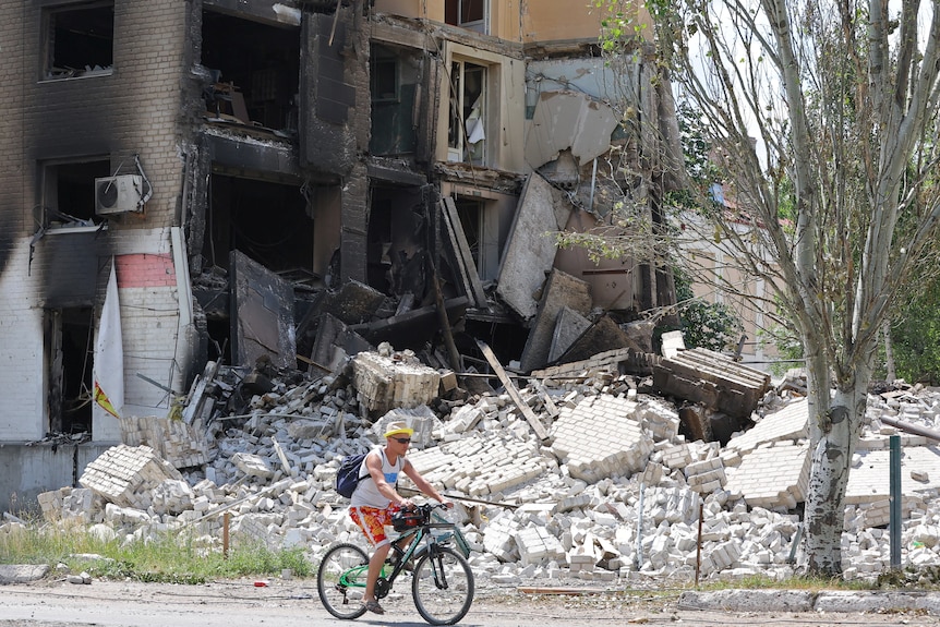 A man rides his bike past rubble and a blown up building in Ukraine