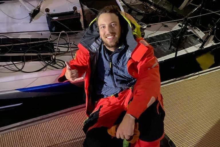 A man wearing a red jacket sits in front of a boat smiling giving the thumbs up