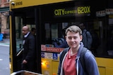 A young man stands in front of a bus