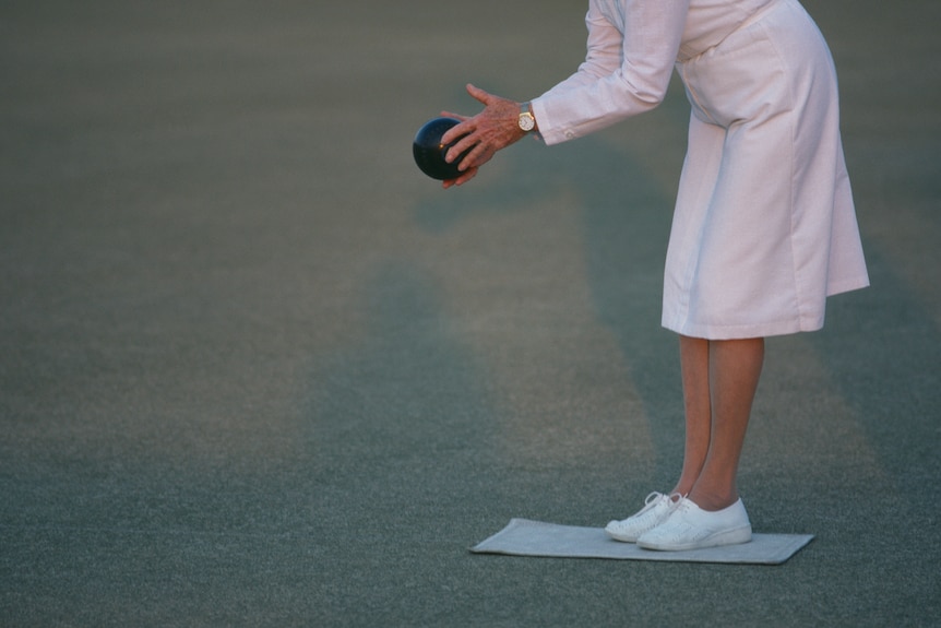 A woman in white leans down and is about to release a bowl.