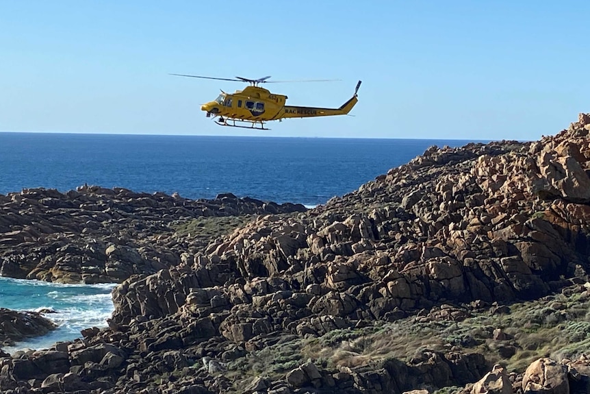 A rescue helicopter hovers along the rocky coastline at Injidup, searching for a person swept from rocks.