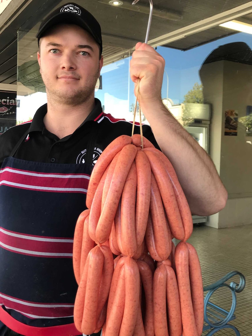 A man in a butcher's apron holding a large haul of freshly made beef sausages.