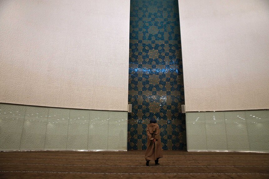 Veiled woman looks at a modern mural design at a mosque's prayer hall.