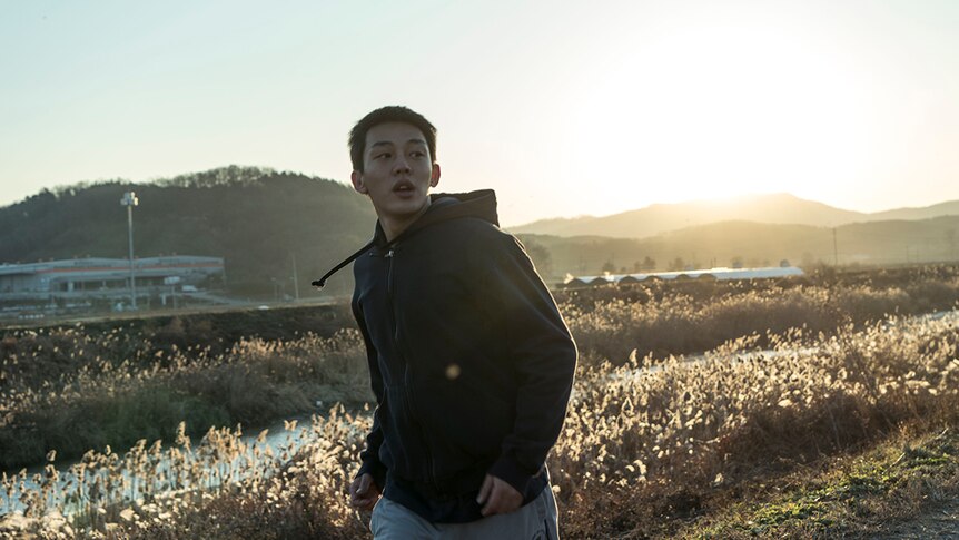 Colour still of Yoo Ah-in jogging in at sunrise in the countryside in 2018 film Burning.