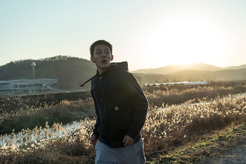 Colour still of Yoo Ah-in jogging in at sunrise in the countryside in 2018 film Burning.