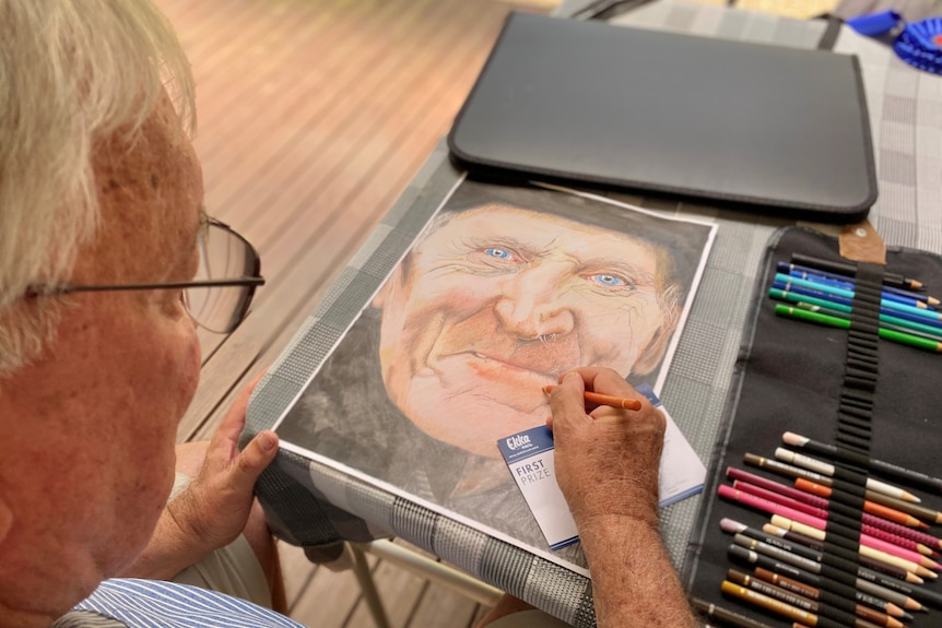 Man drawing a portrait of another man using coloured pencils