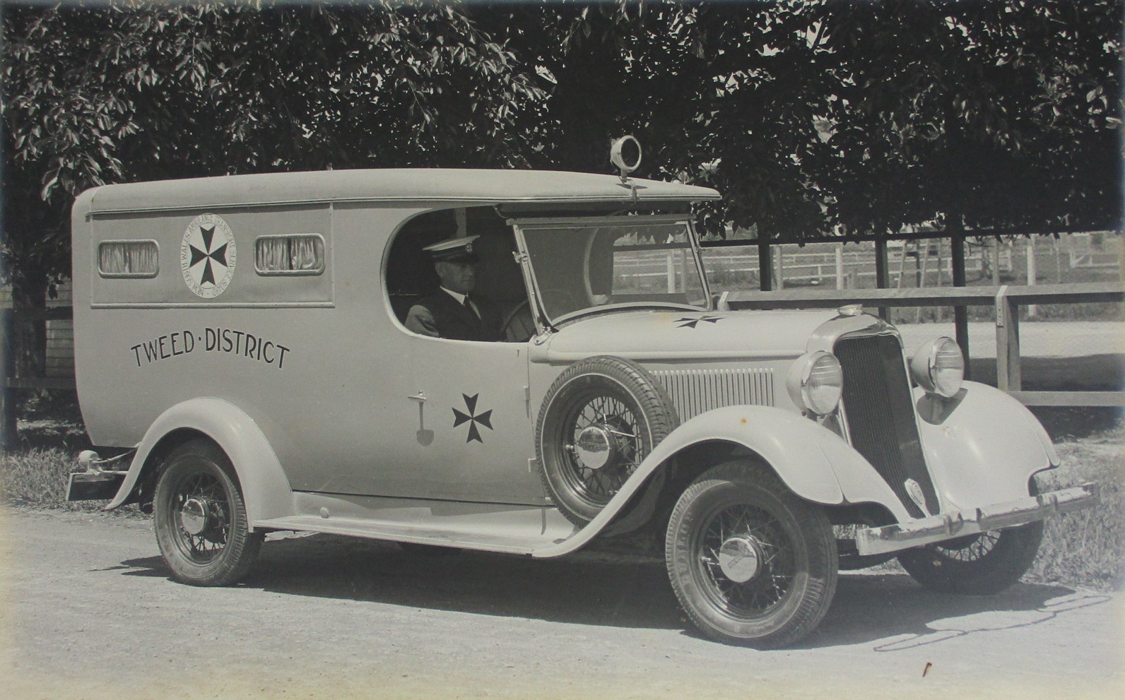 A man sits in an old ambulance, photo taken circa 1925