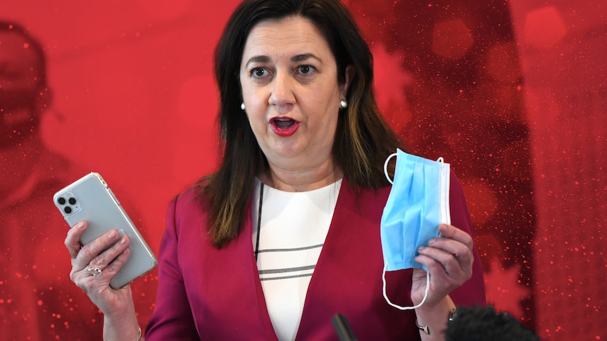 Annastacia Palaszczuk holds a mobile phone and mask over a red graphics background.