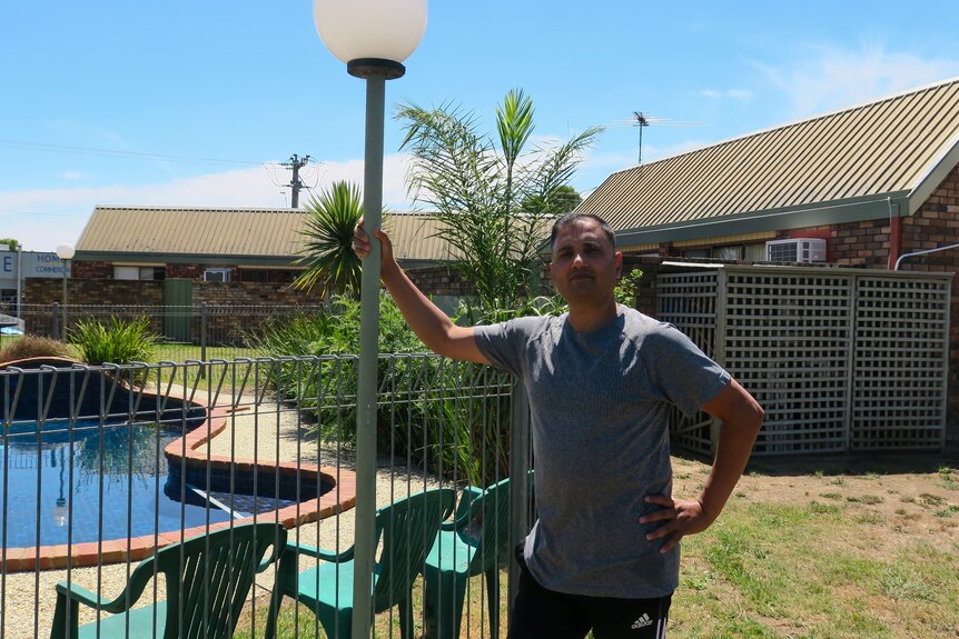 A man in a t-shirt holding a light pole next to a swimming pool