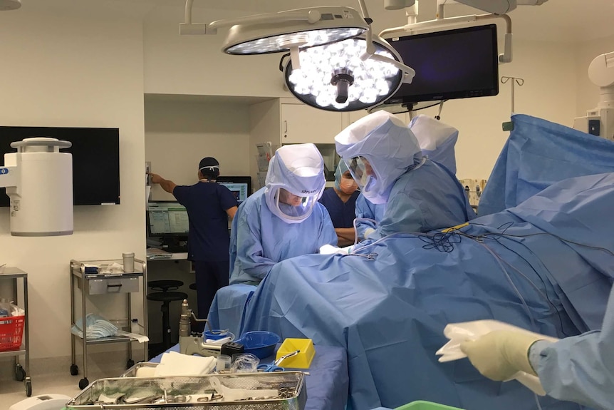 five medical professionals wearing scrubs and protective head gear operate on a person