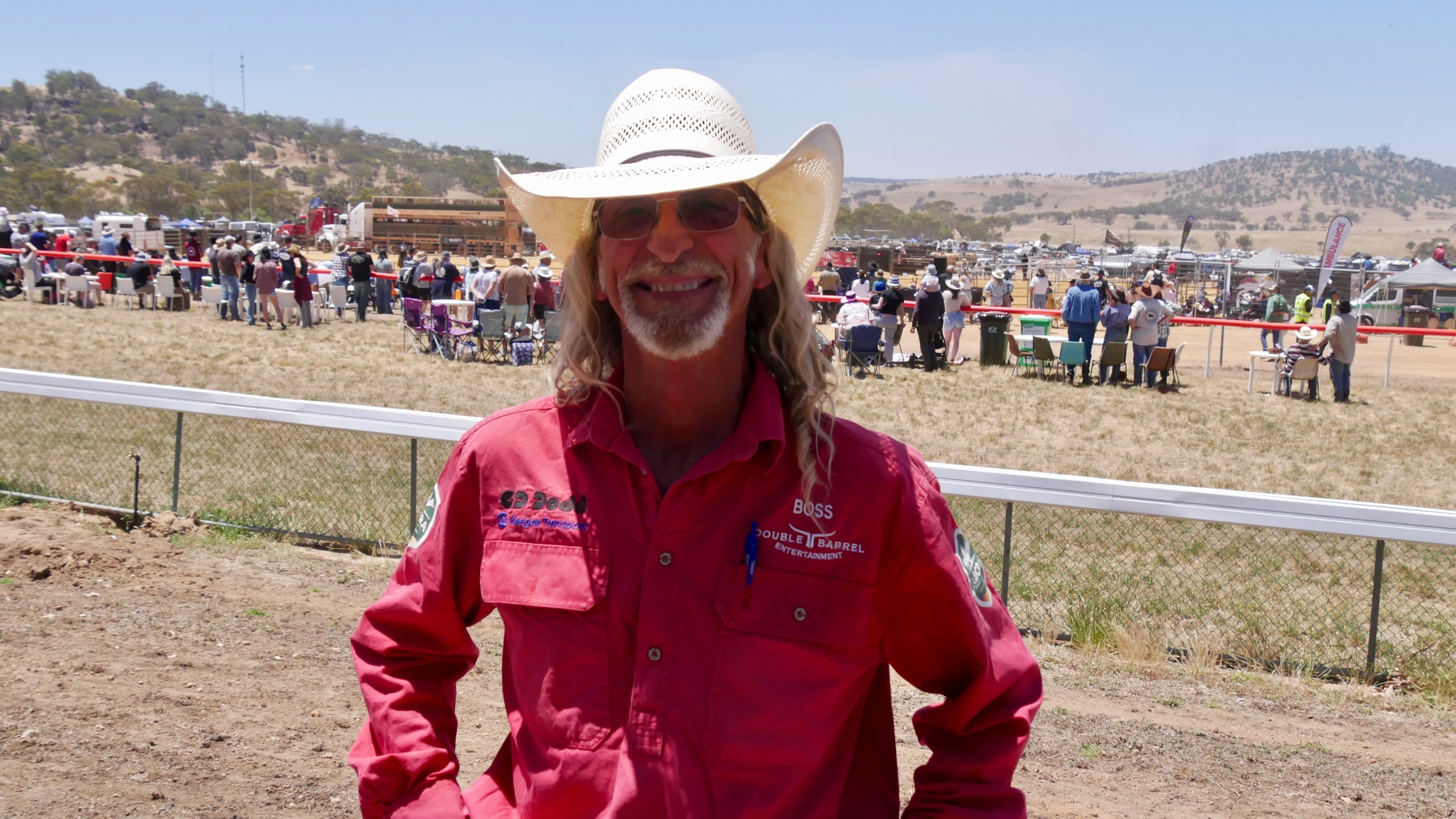 Um homem usando um chapéu de cowboy branco e uma camisa vermelha sorri para a câmera.