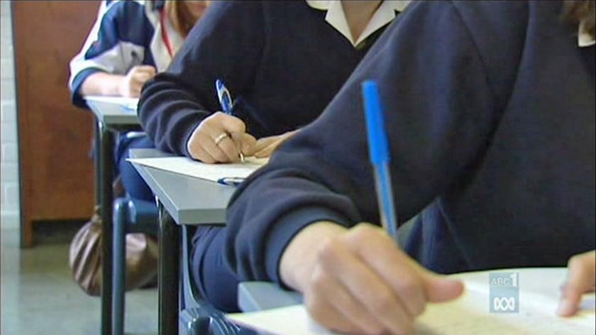 students sitting at desks write on pieces of paper.