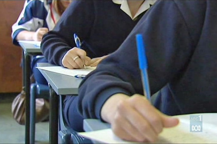 students sitting at desks write on pieces of paper.