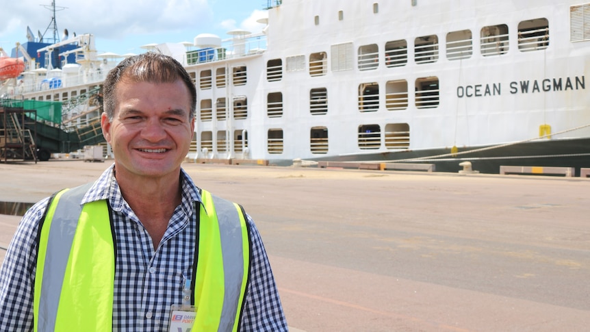 a man with a hi-vis vest on, standing in front of a live export ship.