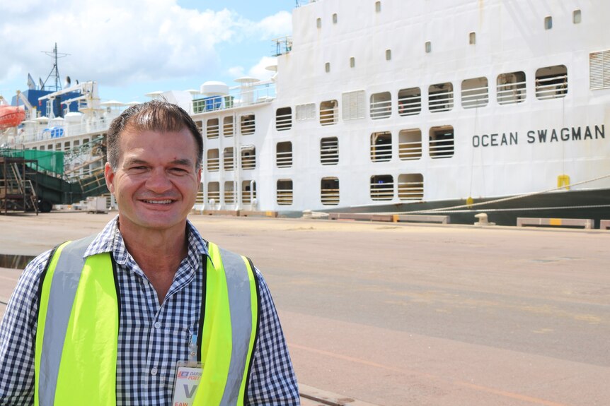 a man with a hi-vis vest on, standing in front of a live export ship.