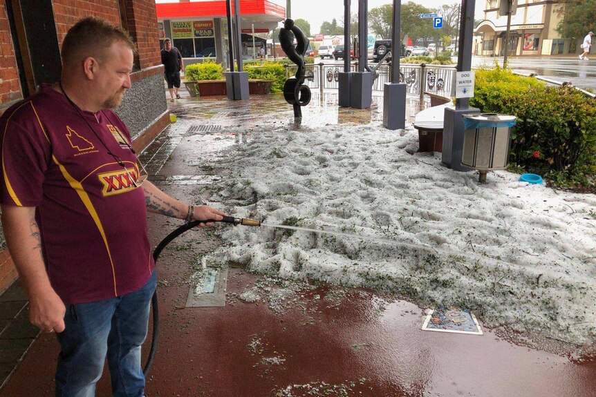 A man hoses down hail dumped on a footpath