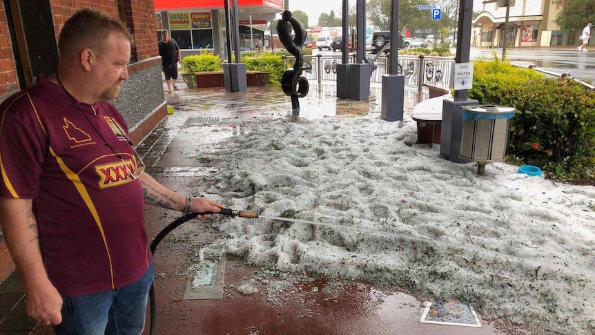 A man hoses down hail dumped on a footpath