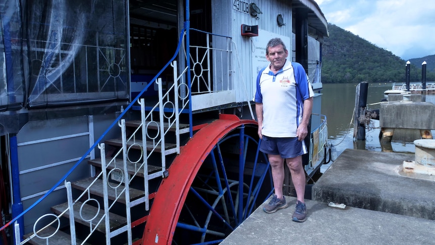 A man standing in front of a a paddlewheeler boat