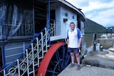 A man standing in front of a a paddlewheeler boat