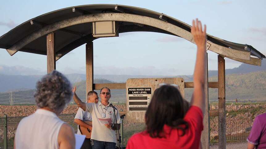 Rev Stuart Hall leads a group in prayer in front of the Ross Dam water level sign